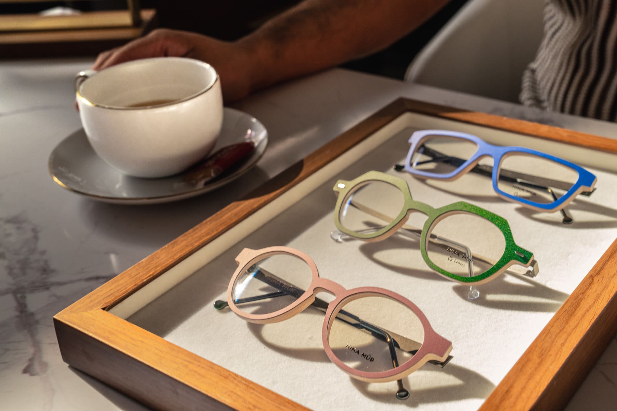 Reaching for a coffee beside a tray of designer frames